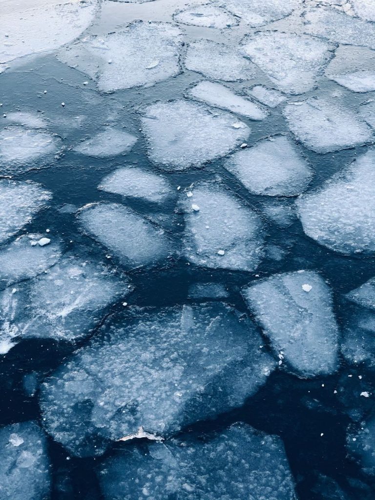 Captivating abstract pattern of frozen ice floes over dark water surface in winter.
