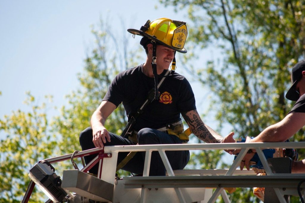 Firefighter in helmet sits on a ladder truck.