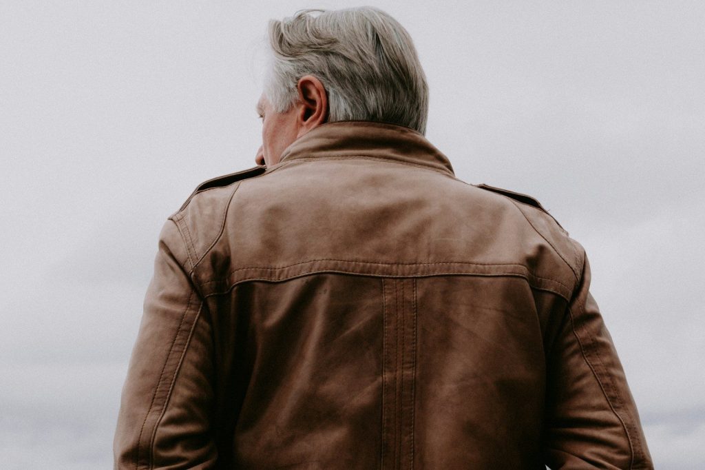 a man in a brown leather jacket standing on a beach