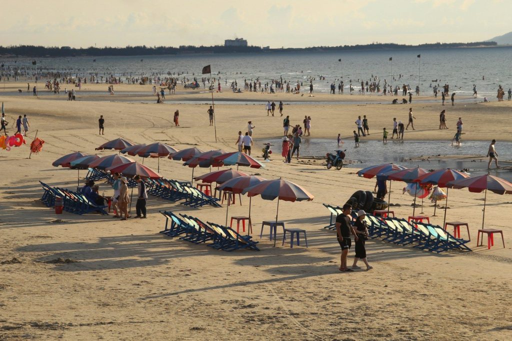 People relaxing on a sandy beach with umbrellas and chairs.