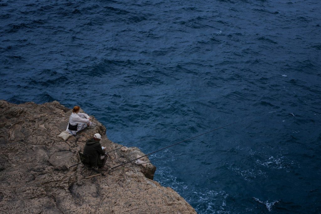 Two people sitting on a rocky cliff overlooking the ocean