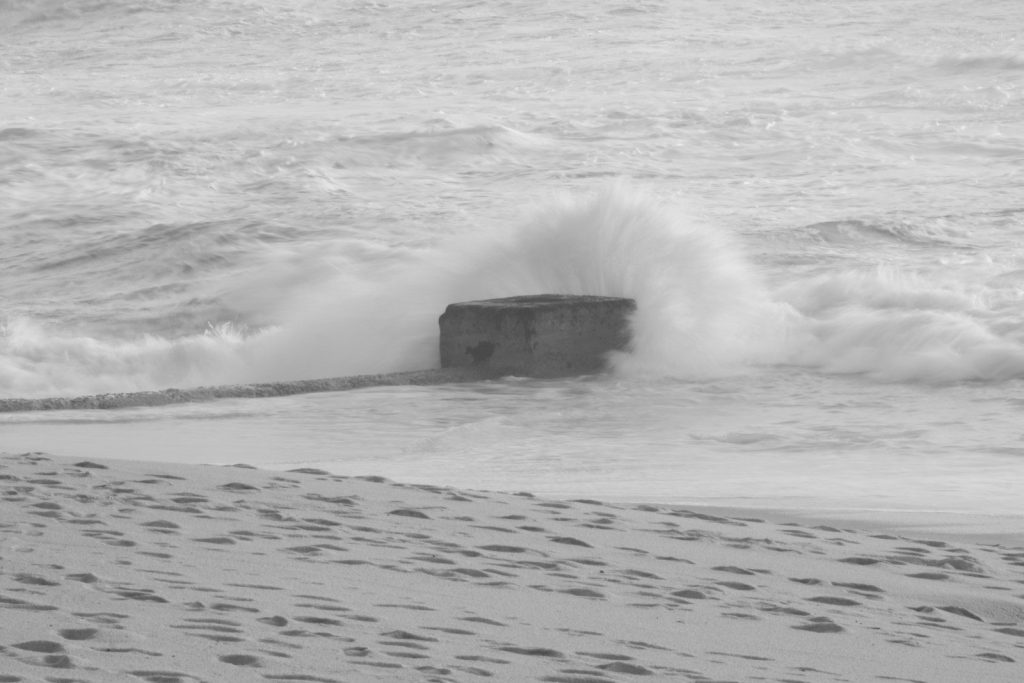 a black and white photo of waves crashing on a rock
